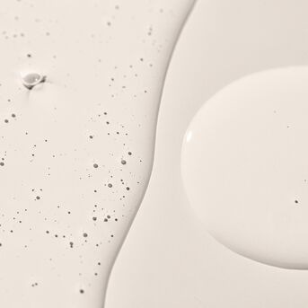 Texture cremosa bianca con piccole macchie scure, ideale per idratare e nutrire la pelle.