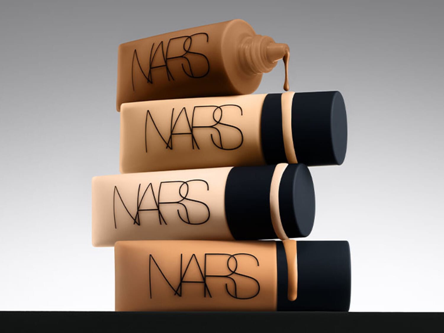 Ecco una pila di fondotinta NARS in diverse tonalità, dai toni chiari a quelli scuri, con confezioni beige e tappi neri.