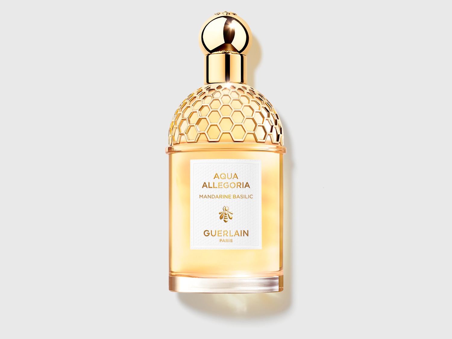 Az Aqua Allegoria Mandarine Basilic parfüm üvegben, arany kupakkal és méhsejt mintázattal, a Guerlain-től.