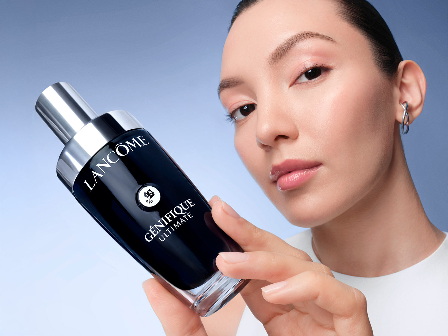 Žena drží v ruke čiernu fľaštičku Lancôme Génifique Ultimate s lesklým strieborným vrchnákom, ktorá sľubuje dokonalú starostlivosť o pleť.