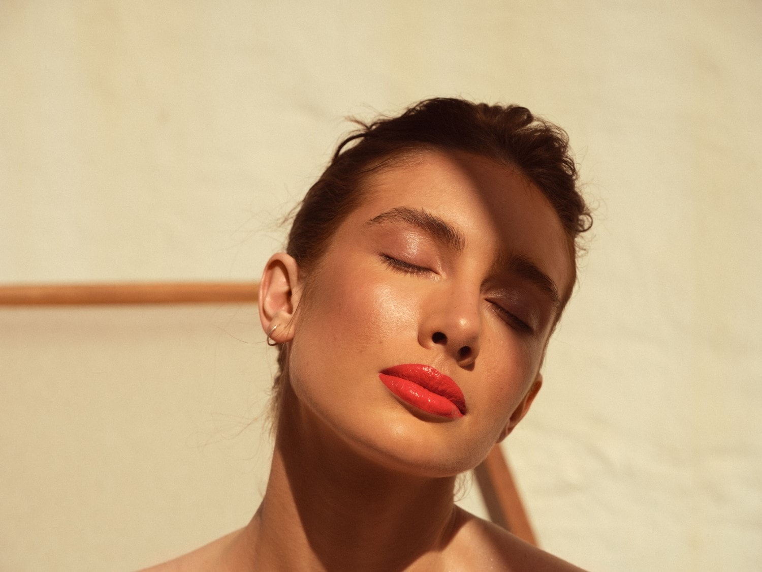 Portrét ženy se zavřenýma očima a lesklými červenými rty, s pletí ozářenou sluncem.