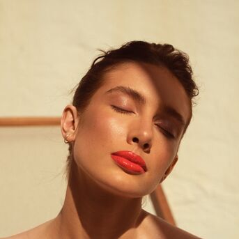 Portrét ženy se zavřenýma očima a sytě červenou rtěnkou, která zvýrazňuje její plné rty.