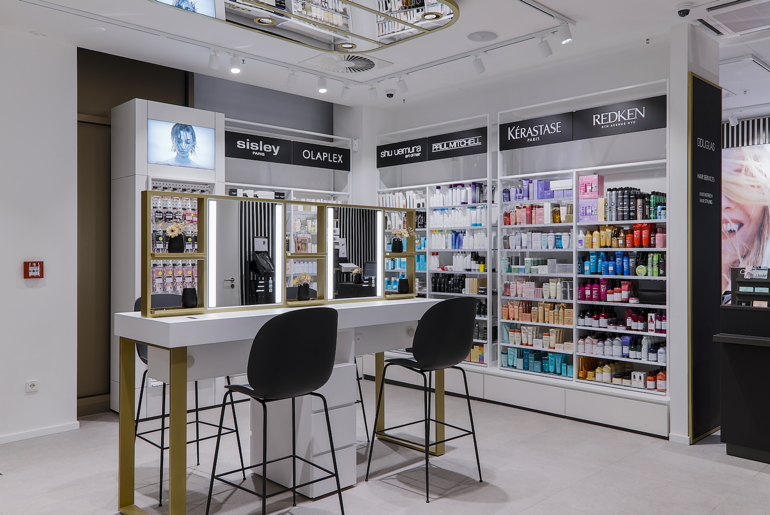 Ein heller, moderner Douglas-Store-Bereich mit Frisiertisch, beleuchteten Spiegeln und Regalen voller Haarpflegeprodukte von Marken wie Sisley, Olaplex, Kérastase und Redken.