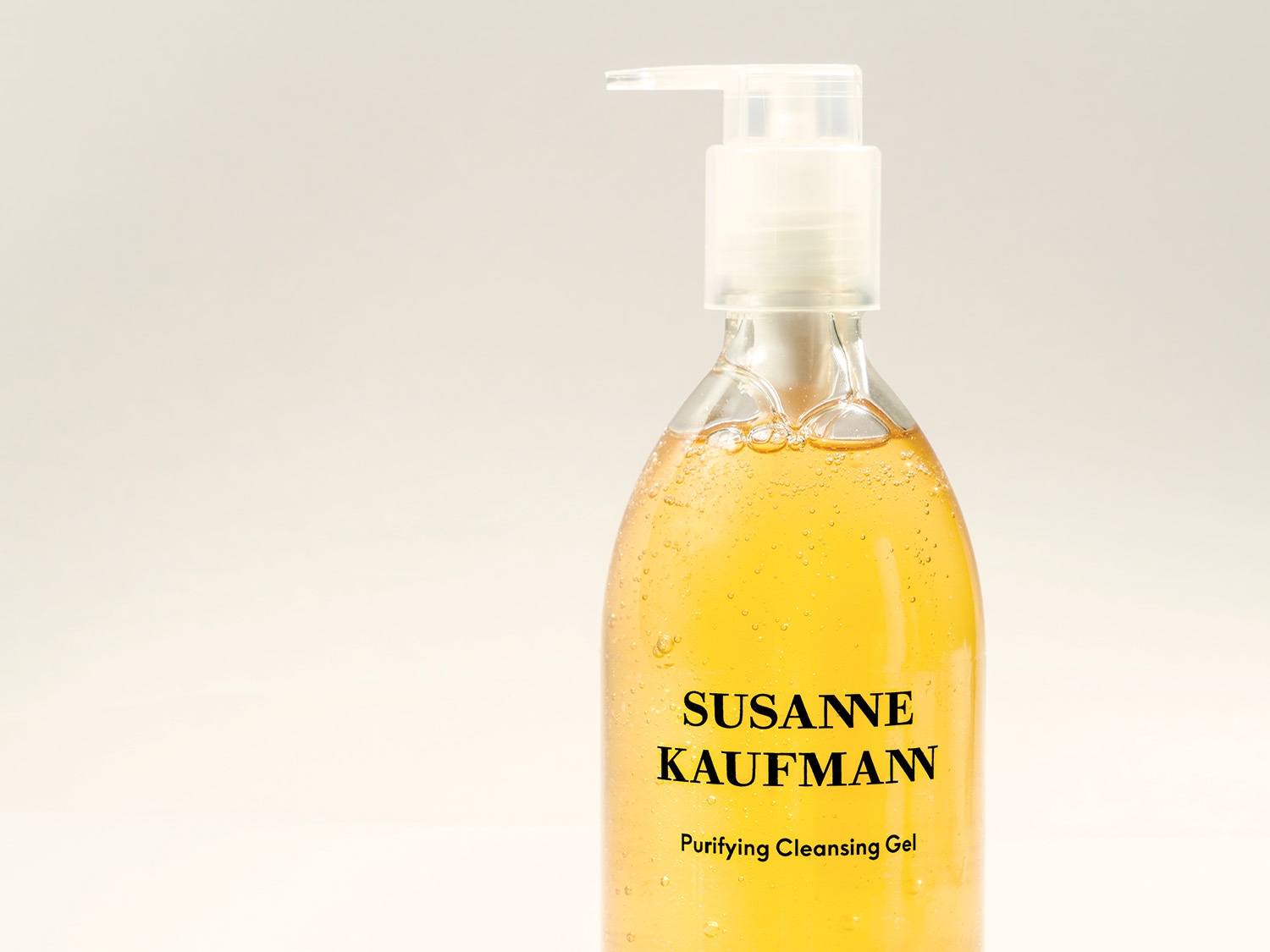 Nahaufnahme einer durchsichtigen Flasche Susanne Kaufmann Purifying Cleansing Gel mit einer bernsteinfarbenen Flüssigkeit und einer Pumpe oben drauf.