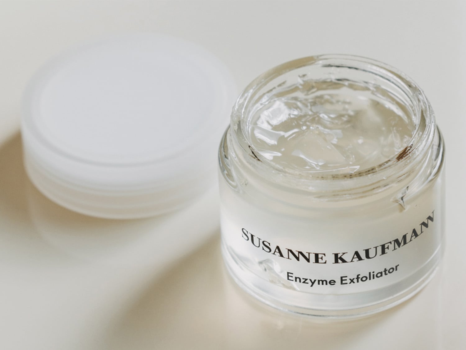 Klarglas-Tiegel mit weißem Etikett, das „Susanne Kaufmann Enzyme Exfoliator“ zeigt, daneben ein weißer Deckel, der eine sanfte und effektive Hauterneuerung verspricht.