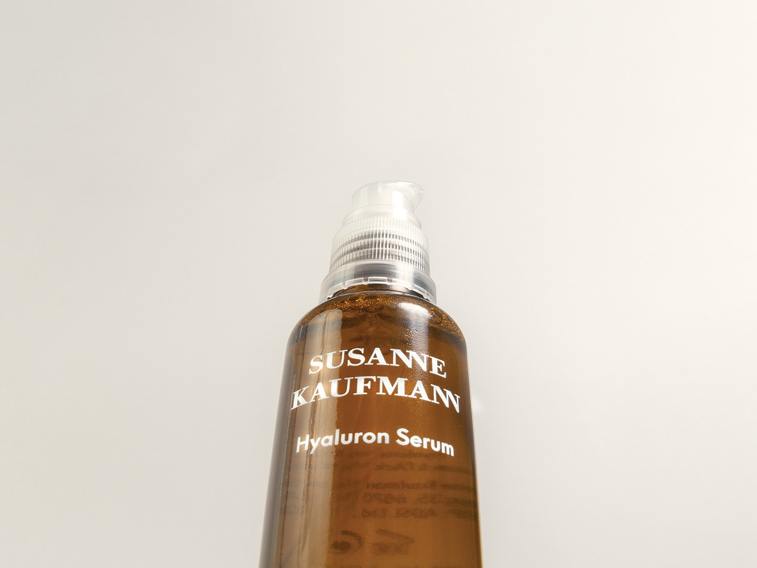 Nahaufnahme einer braunen Glasflasche mit der Aufschrift „Susanne Kaufmann Hyaluron Serum“ und einem durchsichtigen Pumpspender.