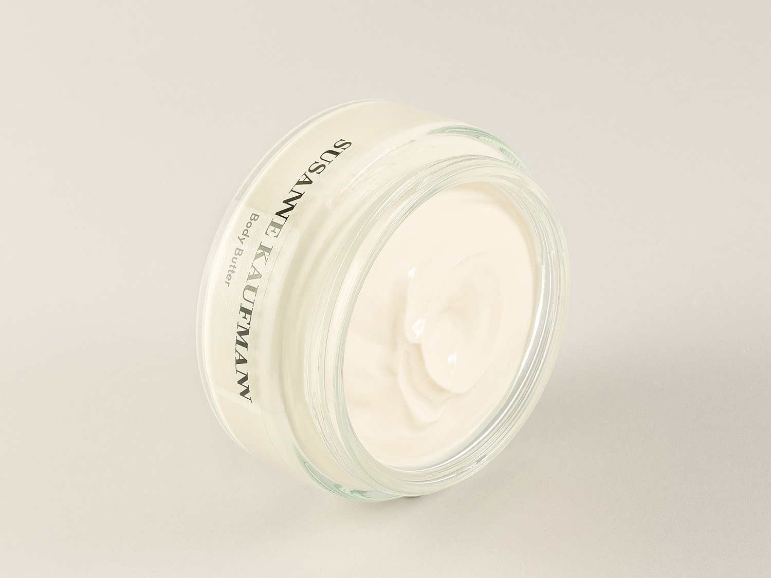 Nahaufnahme einer durchsichtigen Glasdose mit weißer Körperbutter von Susanne Kaufmann, die eine reichhaltige Textur für intensive Feuchtigkeitspflege zeigt.
