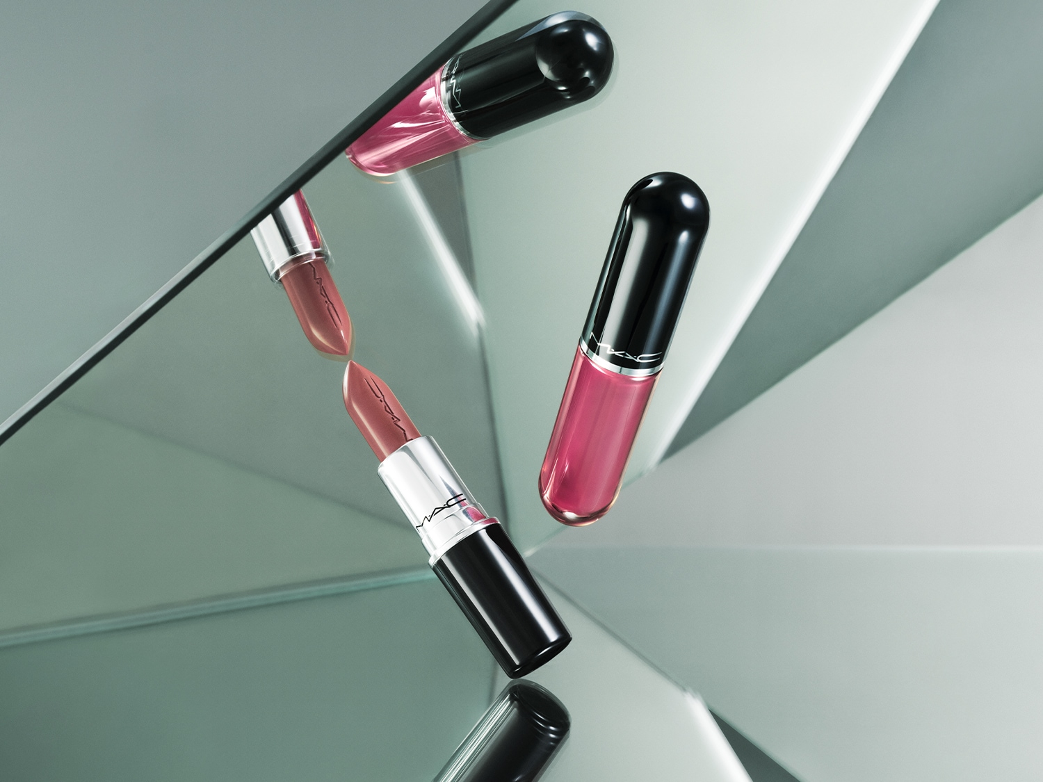 Dvě rtěnky MAC, jedna v odstínu nude a druhá v růžové barvě, jsou zobrazeny na zrcadlovém povrchu, který odráží jejich elegantní design.
