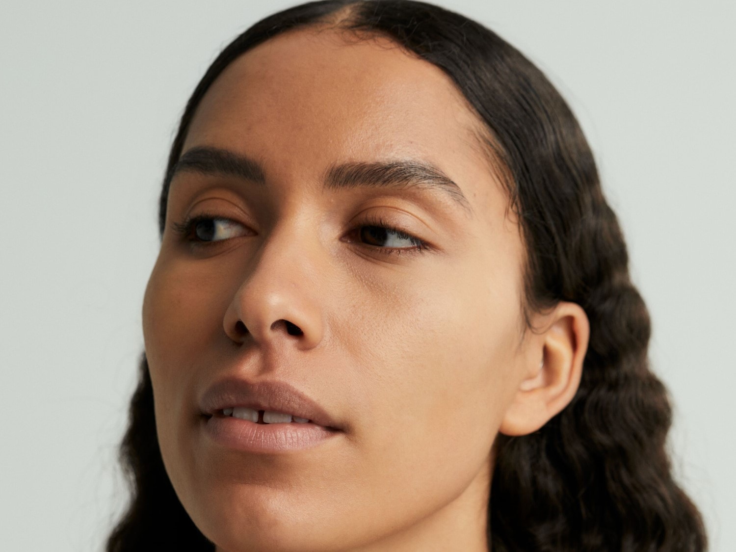Detailný pohľad na tvár ženy s hnedými očami, tmavými vlnitými vlasmi a hladkou pleťou.