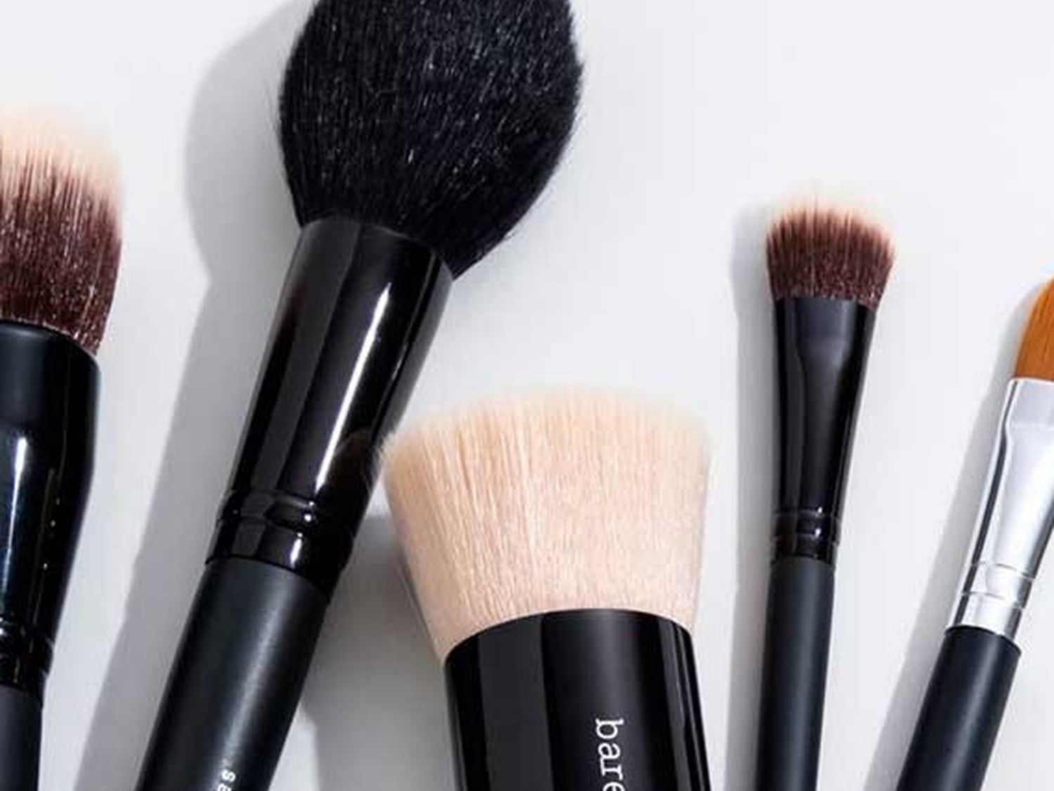 Na białym tle leżą pędzle do makijażu z czarnymi rączkami i różnymi główkami, od dużych i puszystych po małe i precyzyjne.
