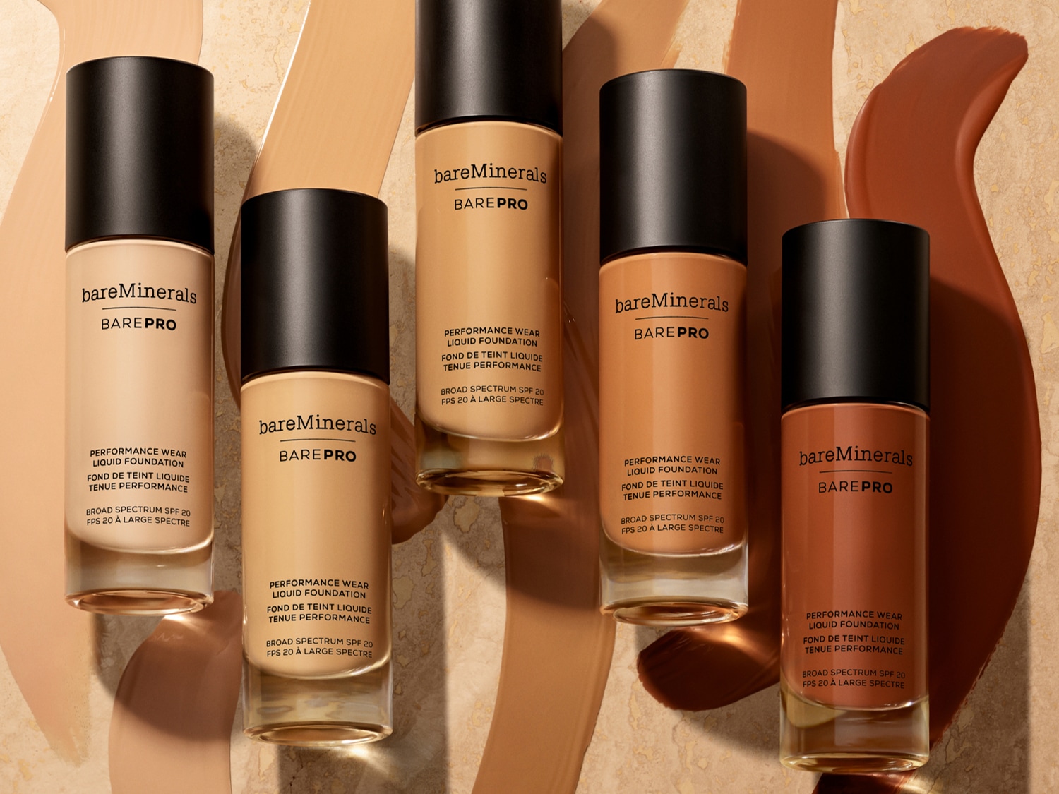 Różne odcienie podkładu w płynie BareMinerals BarePro z czarnymi zakrętkami, ułożone na tle z smugami podkładu, oferują szeroki wybór dopasowany do każdej karnacji.