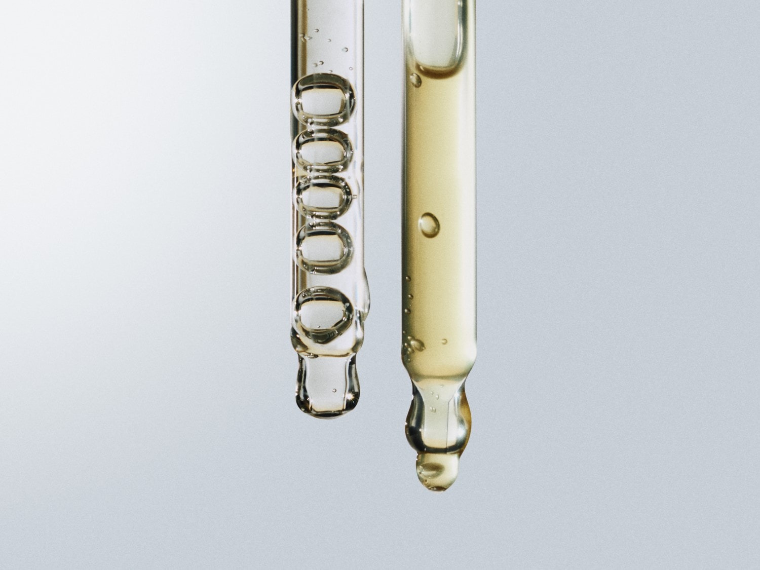 Nahaufnahme von zwei Pipetten, eine gefüllt mit klarer Flüssigkeit und die andere mit goldfarbener Flüssigkeit, die die Textur und Farbe der Seren hervorhebt.