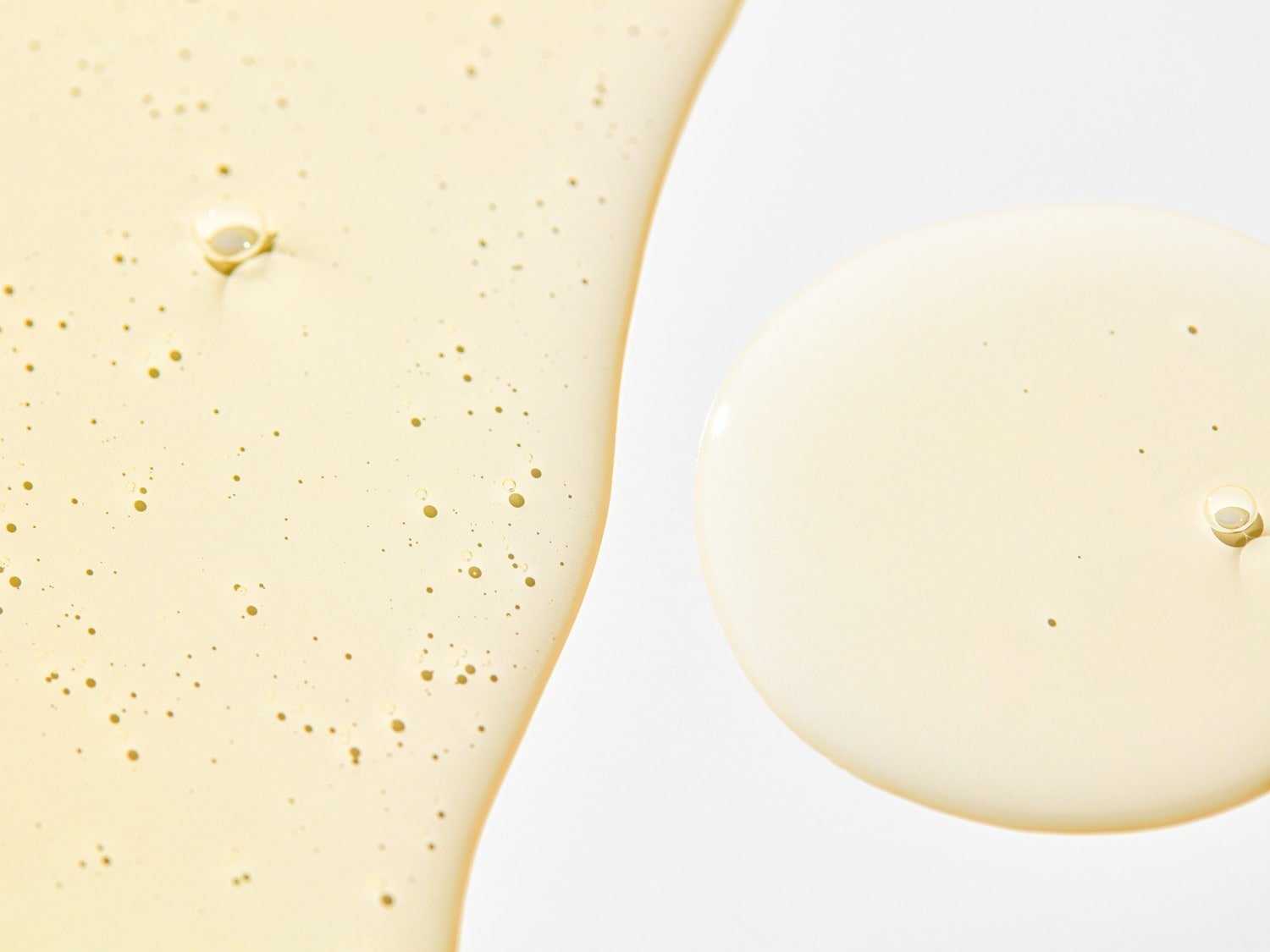 Nahaufnahme von Serumtropfen, die eine helle, leicht gelbliche Textur mit kleinen Bläschen auf einer glatten, weißen Oberfläche zeigen.