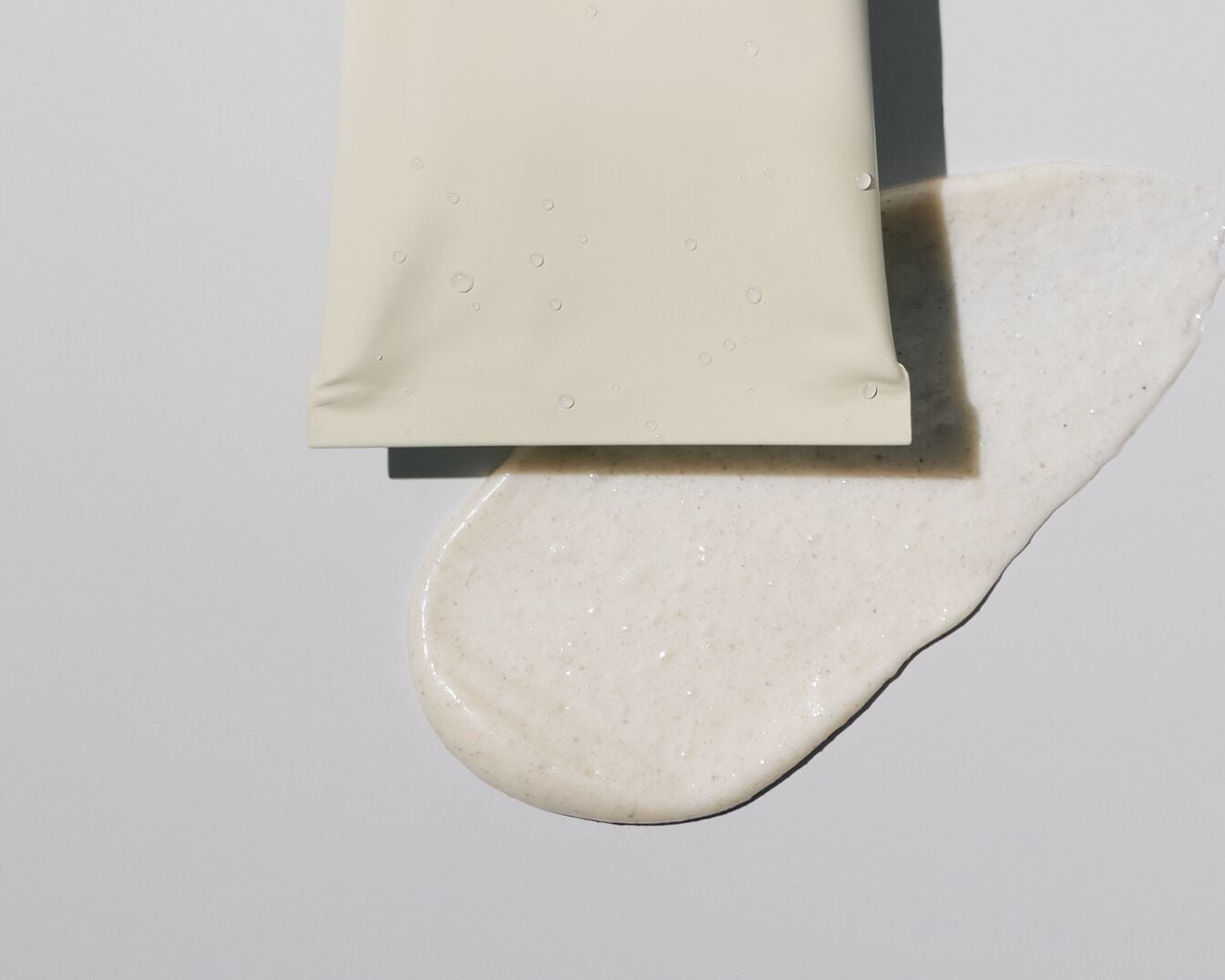 Nahaufnahme einer hellen Tube mit ein paar Wassertropfen daneben, die eine cremige, schaumige Substanz freisetzt.