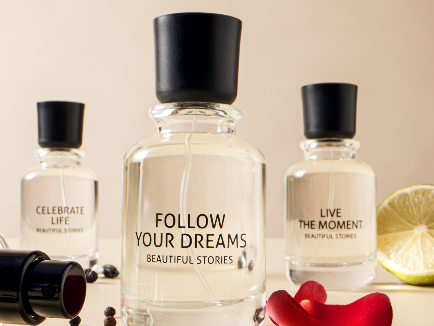Három átlátszó üvegben parfümök láthatók, fekete kupakkal, melyeken a következő feliratok állnak: „Ünnepeld az életet”, „Kövesd az álmaidat” és „Éld meg a pillanatot”.