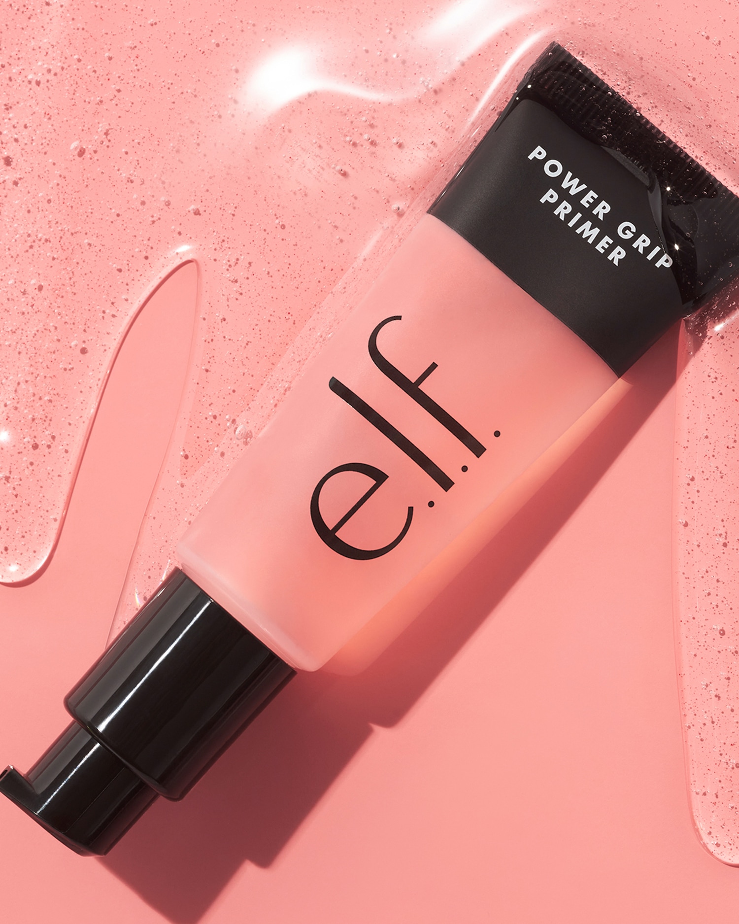 De e.l.f. Power Grip Primer in een roze tube met zwarte details, ligt op een roze achtergrond met een glanzende textuur.