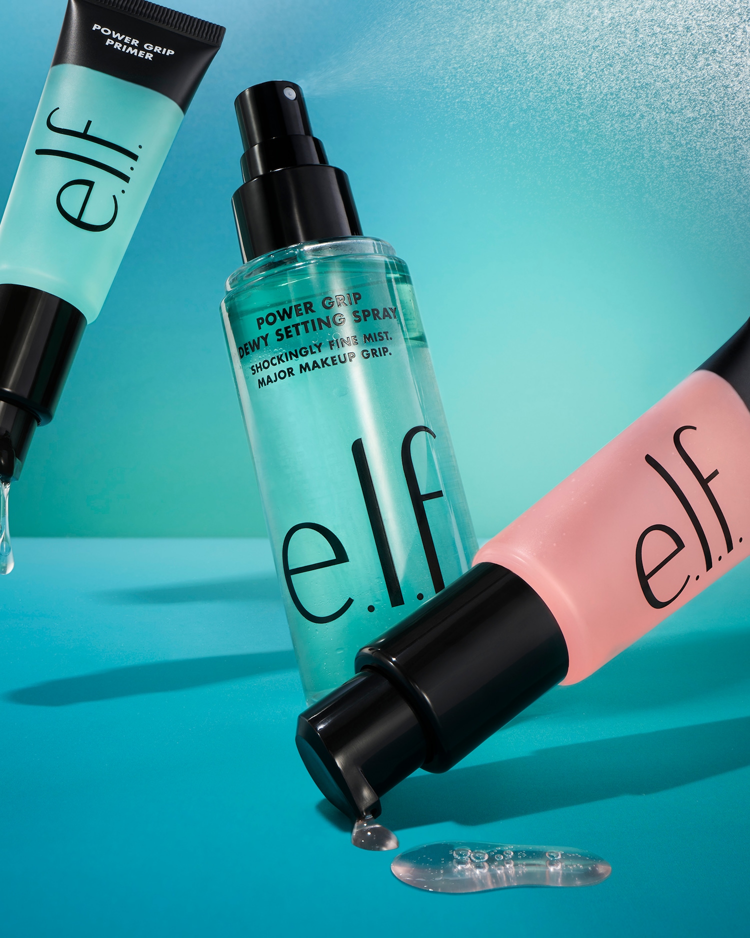 Drie e.l.f. producten staan op een blauwe achtergrond: een mintgroene Power Grip Primer tube, een Power Grip Dewy Setting Spray fles en een roze tube.