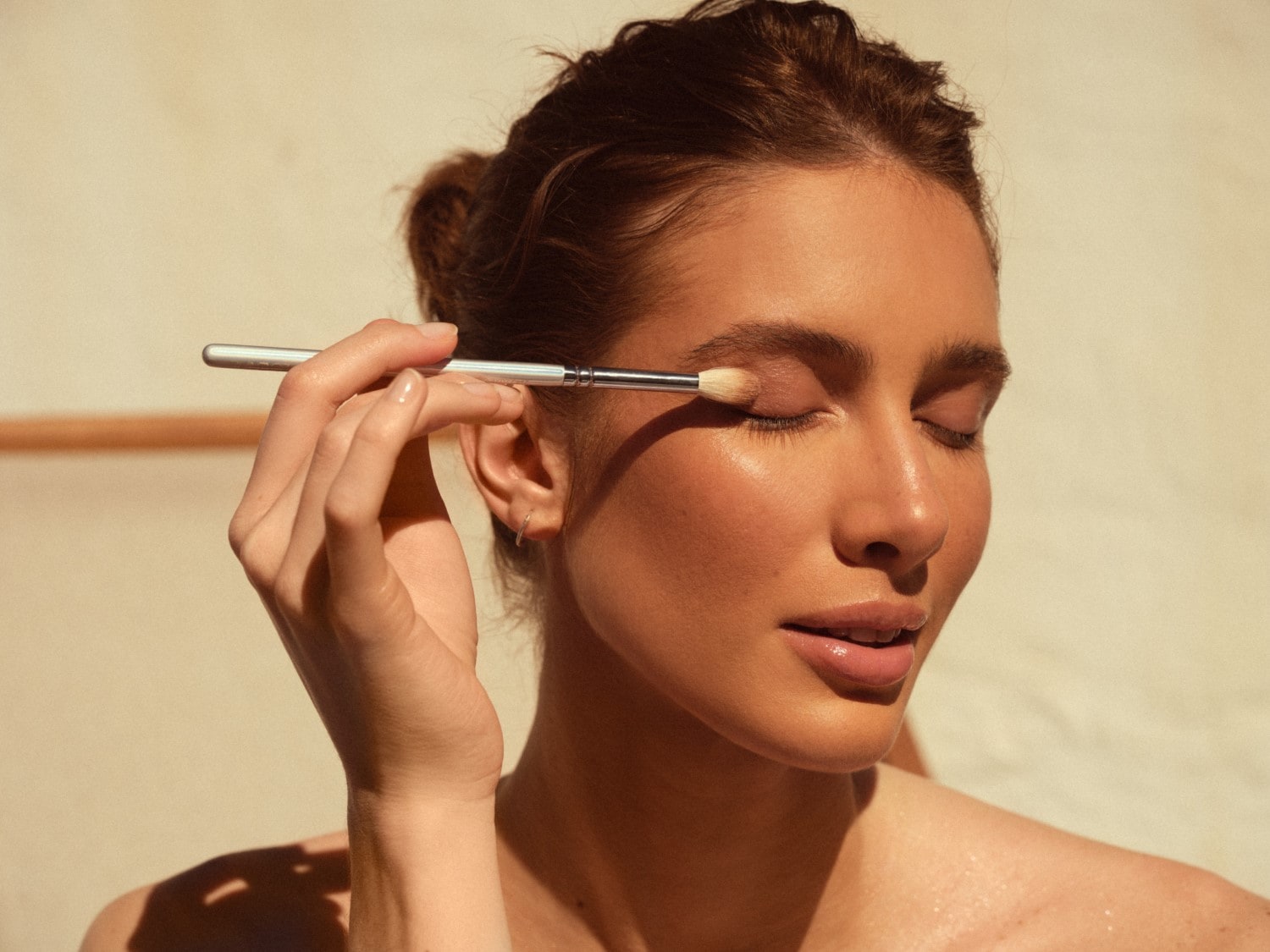 Žena si nanáša svetlohnedé očné tiene strieborným štetcom, aby dosiahla dokonalý vzhľad.