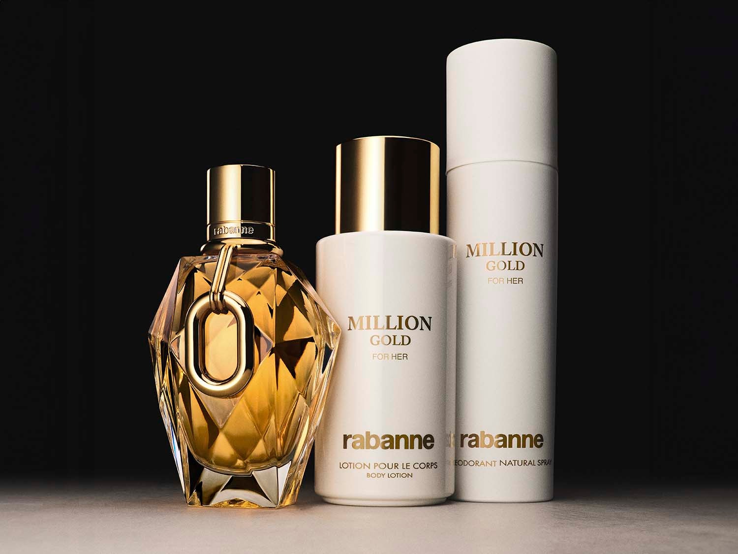 Abgebildet ist eine Kollektion von Rabanne 'Million Gold for Her'-Produkten, darunter ein Parfüm in einem facettierten Goldflakon, eine Körperlotion in einer weißen Flasche und ein Deodorant-Spray.