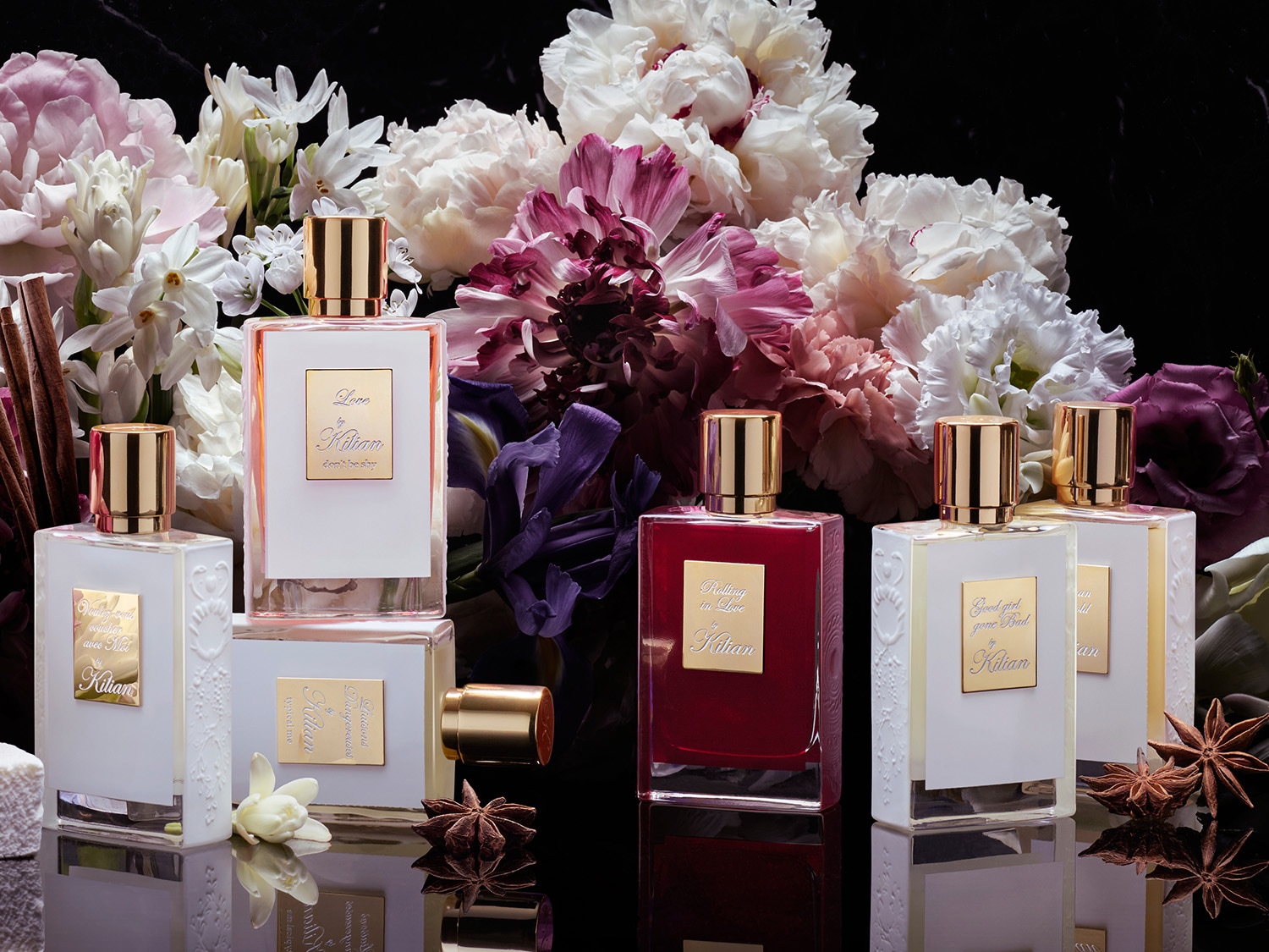 Különböző Kilian parfümök láthatók virágokkal a háttérben, köztük a Love by Kilian és a Good girl gone Bad, elegáns üvegekben, arany kupakkal.