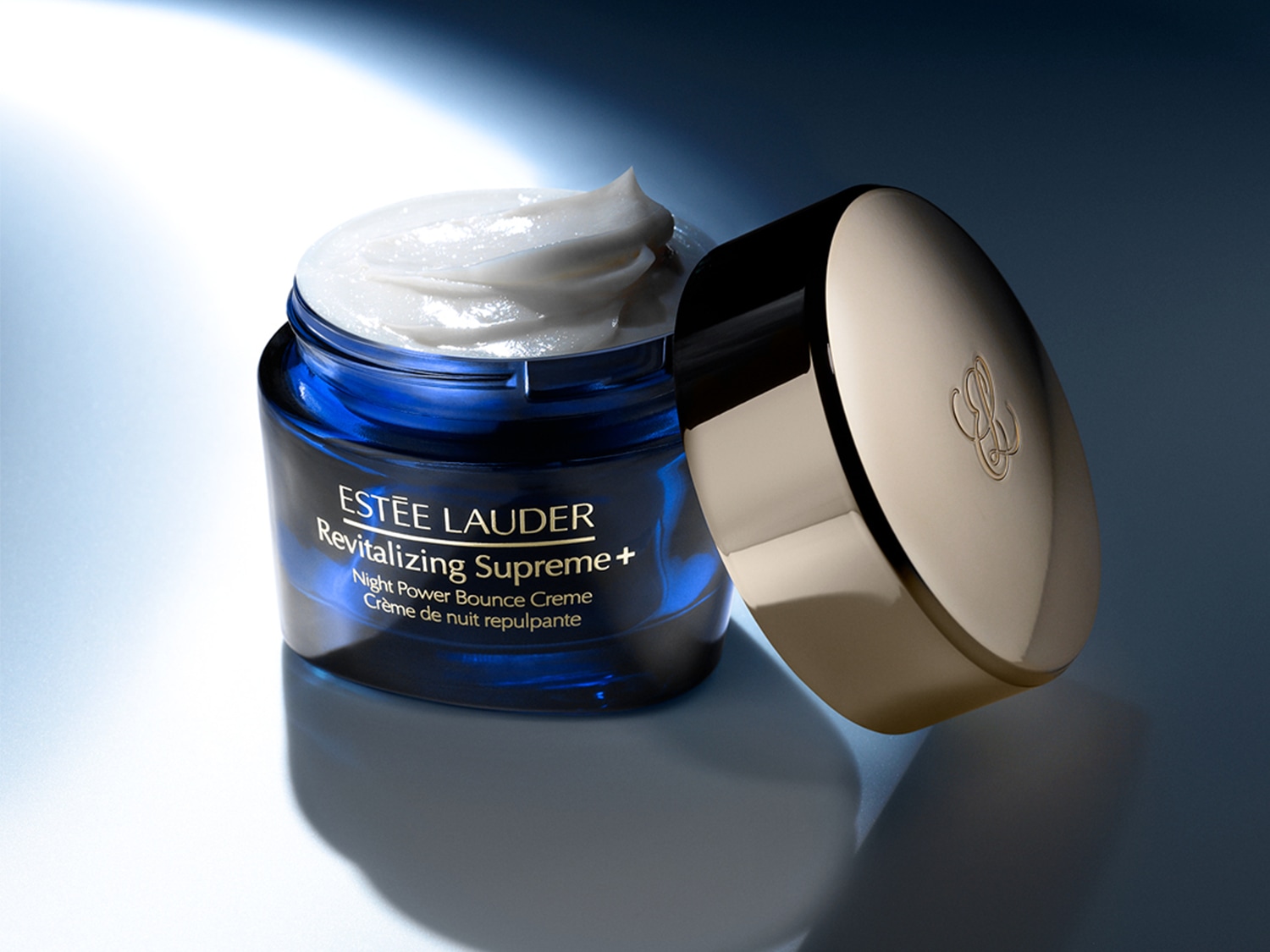Az Estée Lauder Revitalizing Supreme+ Night Power Bounce Creme éjszakai krém kék tégelyben, arany színű kupakkal, tele fehér színű krémmel.