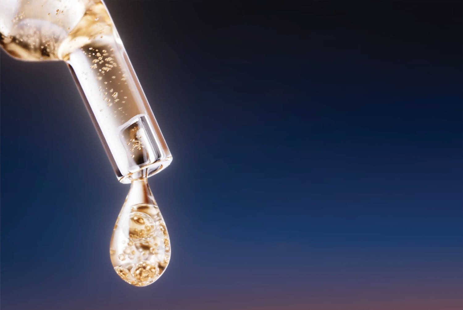 Arany színű szérumcsepp esik egy üvegpipettából, amely tele van apró buborékokkal, sötétkék háttér előtt.