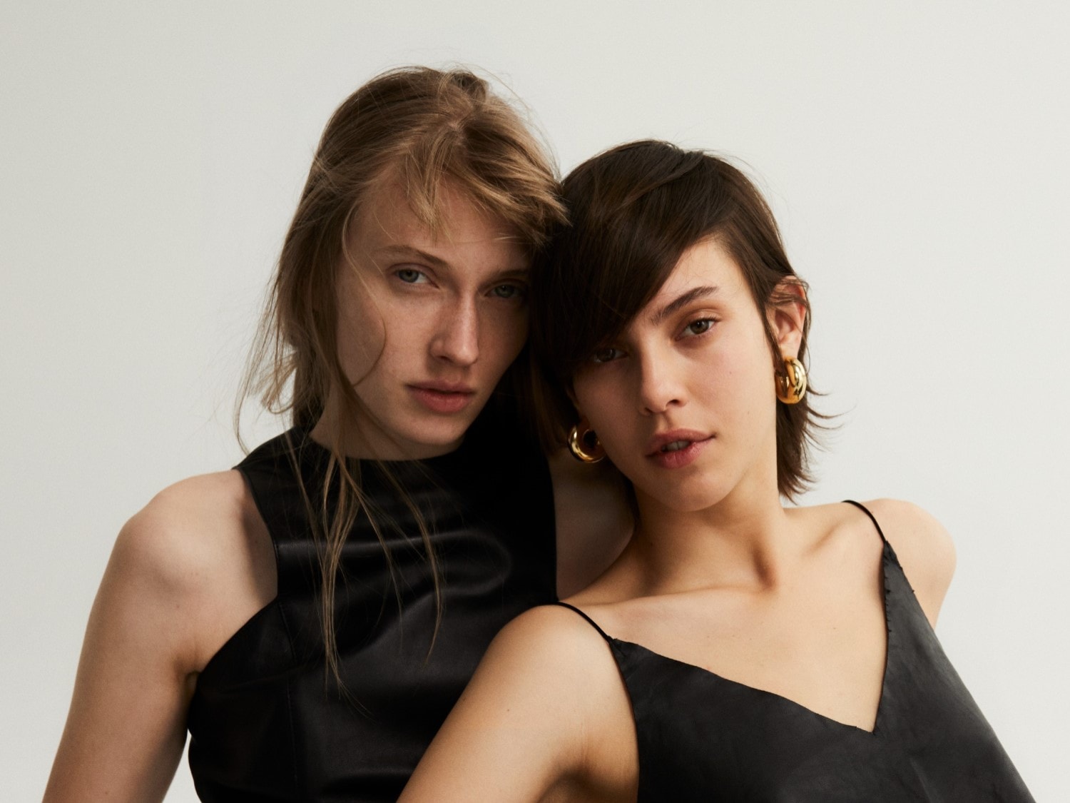 Két nő portréja, akik fekete ruhát viselnek és arany fülbevalót viselnek, a minimalista elegancia megtestesítői.