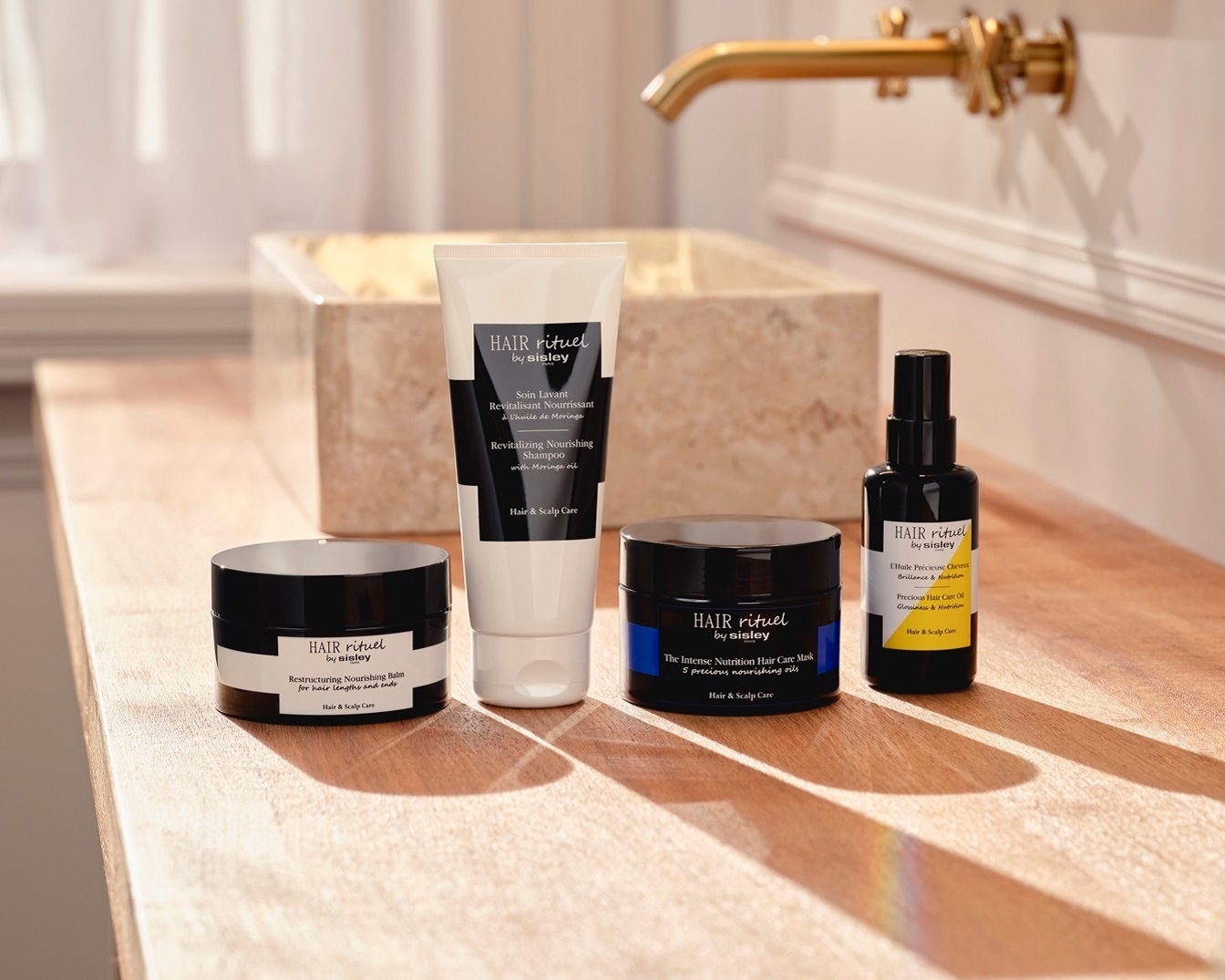 Cztery produkty do pielęgnacji włosów Hair Rituel by Sisley, w tym szampon odżywczy, balsam restrukturyzujący, maska odżywcza i olejek, stoją na drewnianej powierzchni.