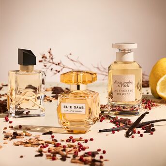 Tři flakony parfémů od YSL, Elie Saab a Abercrombie & Fitch v odstínech zlata a béže, doplněné o citron a koření.