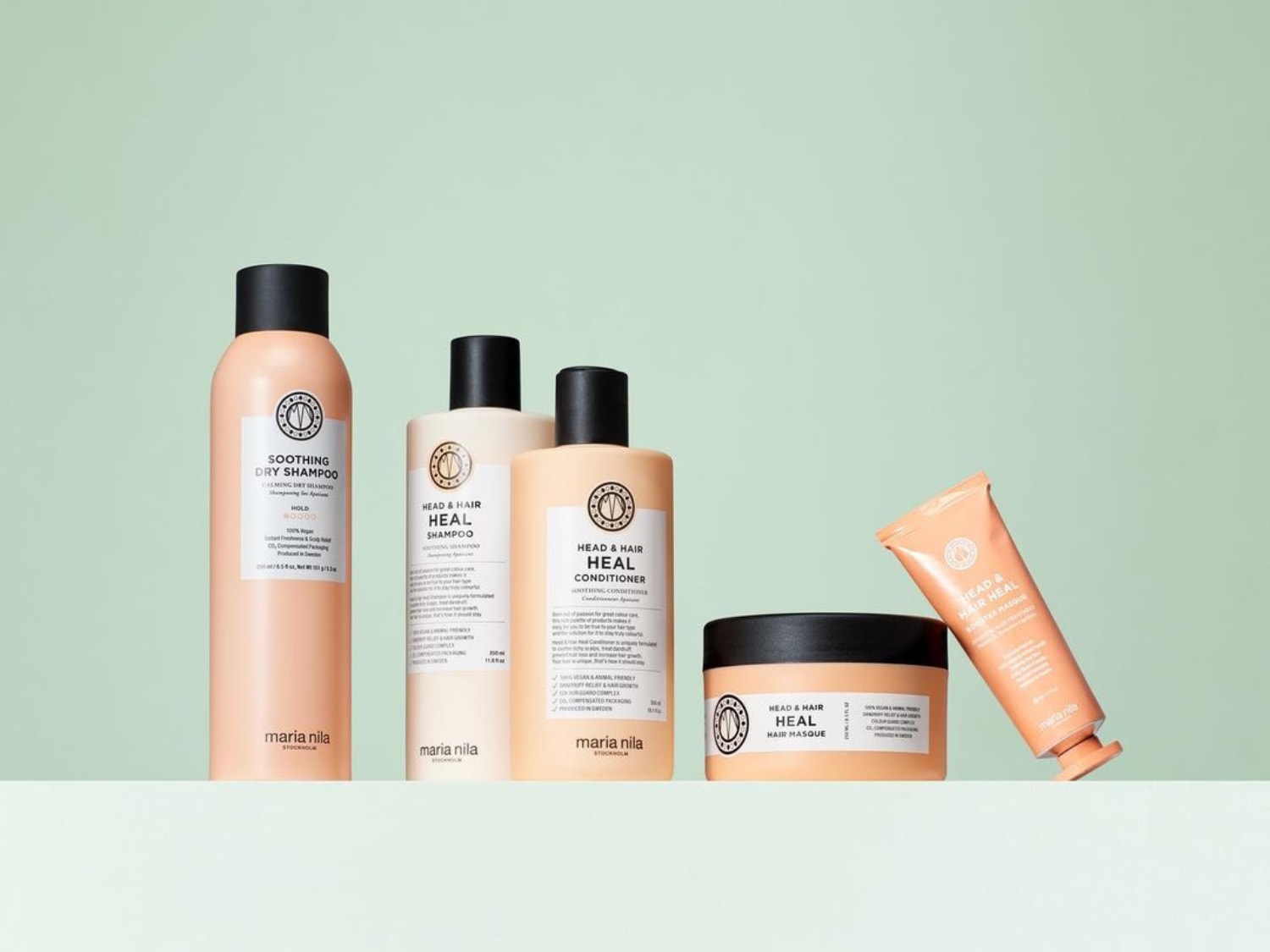 Eine Auswahl an Maria Nila Head & Hair Heal Produkten, darunter Trockenshampoo, Shampoo, Conditioner und Haarmaske in hellpfirsichfarbenen Verpackungen mit schwarzen Akzenten.