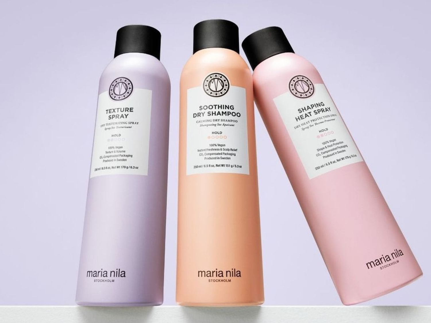 Drei Maria Nila Haarsprays in Pastellfarben: Texturspray in Lila, Trockenshampoo in Pfirsich und Hitzespray in Rosa, alle mit veganer Formel für unterschiedliche Stylingbedürfnisse.