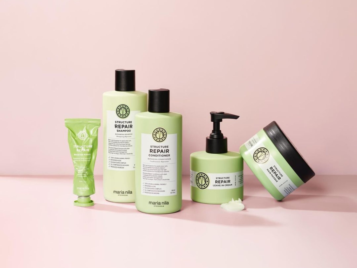 Eine Kollektion von Maria Nila Structure Repair-Produkten in hellgrünen Verpackungen, darunter Shampoo, Spülung, Haarmaske und Leave-in-Creme, die auf einer rosa Oberfläche für die Reparatur und Pflege der Haare präsentiert werden.