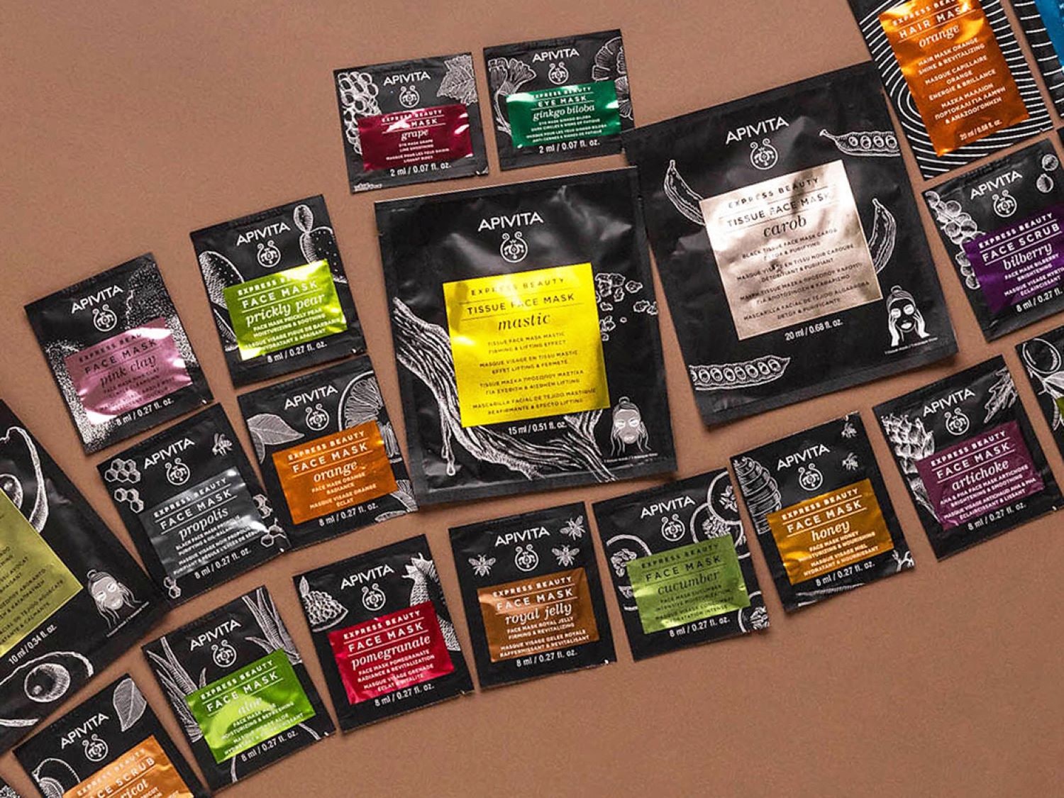 Descubre la variedad de mascarillas faciales Apivita, desde arcilla rosa hasta granada, cada una en un empaque individual negro con detalles de ingredientes.
