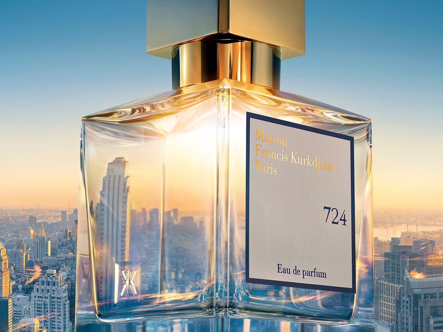 Nahaufnahme des Maison Francis Kurkdjian Paris 724 Eau de Parfum Flakons mit goldenem Verschluss vor einer Skyline im goldenen Licht.