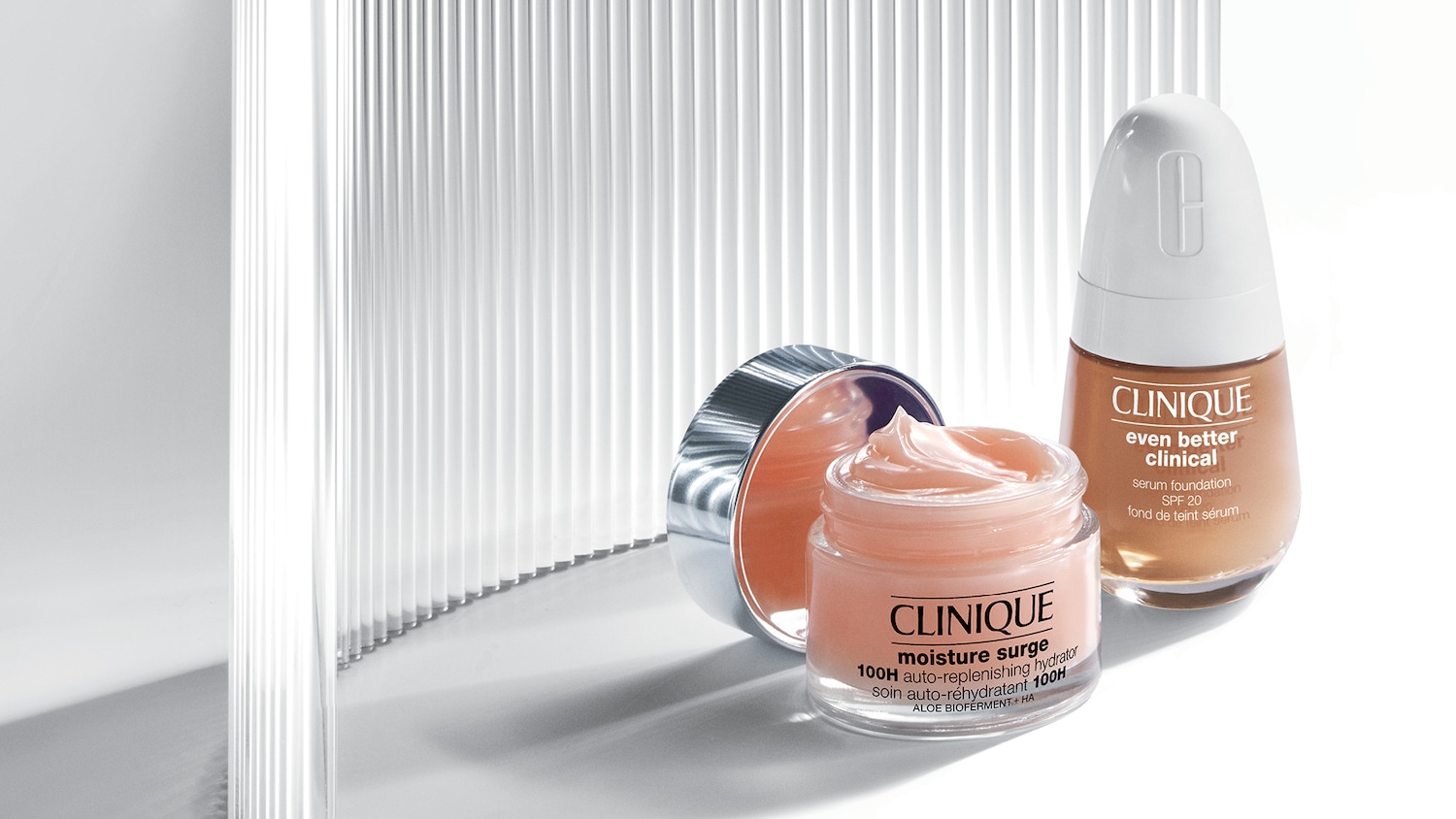 Clinique Moisture Surge 100H auto-replenishing hydrator in een heldere pot met een zilveren deksel, naast Clinique Even Better Clinical serum foundation SPF 20 in een bruine fles.