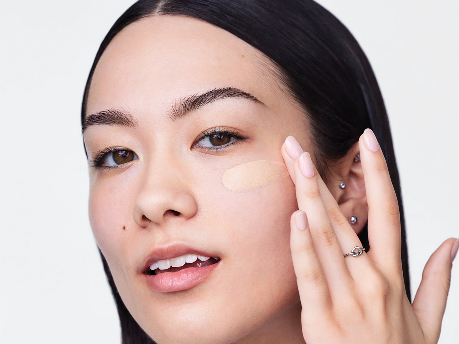 Een vrouw met donker haar brengt met haar vingers een beige foundation aan op haar gezicht.