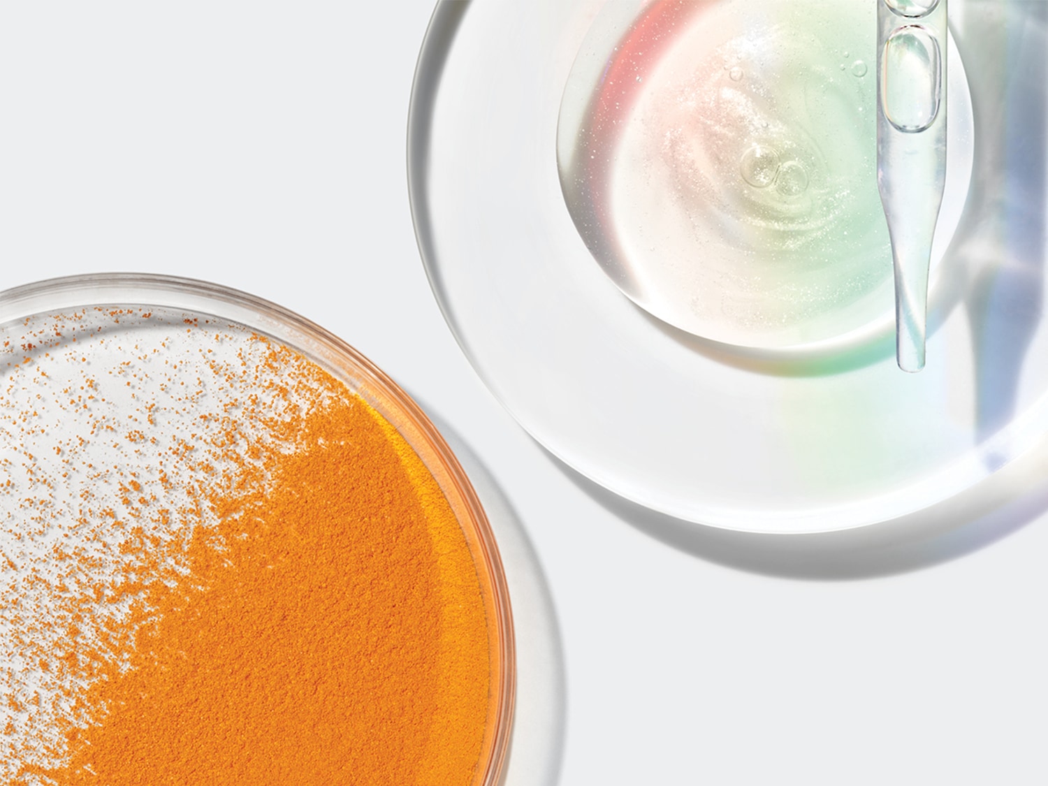 Bovenaanzicht van een oranje poeder in een petrischaal en een heldere vloeistof met een pipet, die de ingrediënten voor een huidverzorgingsproduct laten zien.