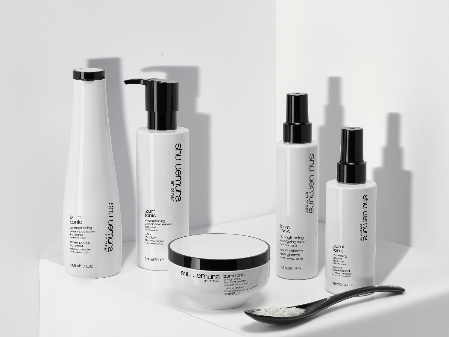 Řada produktů Shu Uemura Art of Hair Izumi Tonic v bílých obalech s černými detaily, včetně šamponu, kondicionéru, tonika a séra, které posilují vlasy díky rýžové vodě.