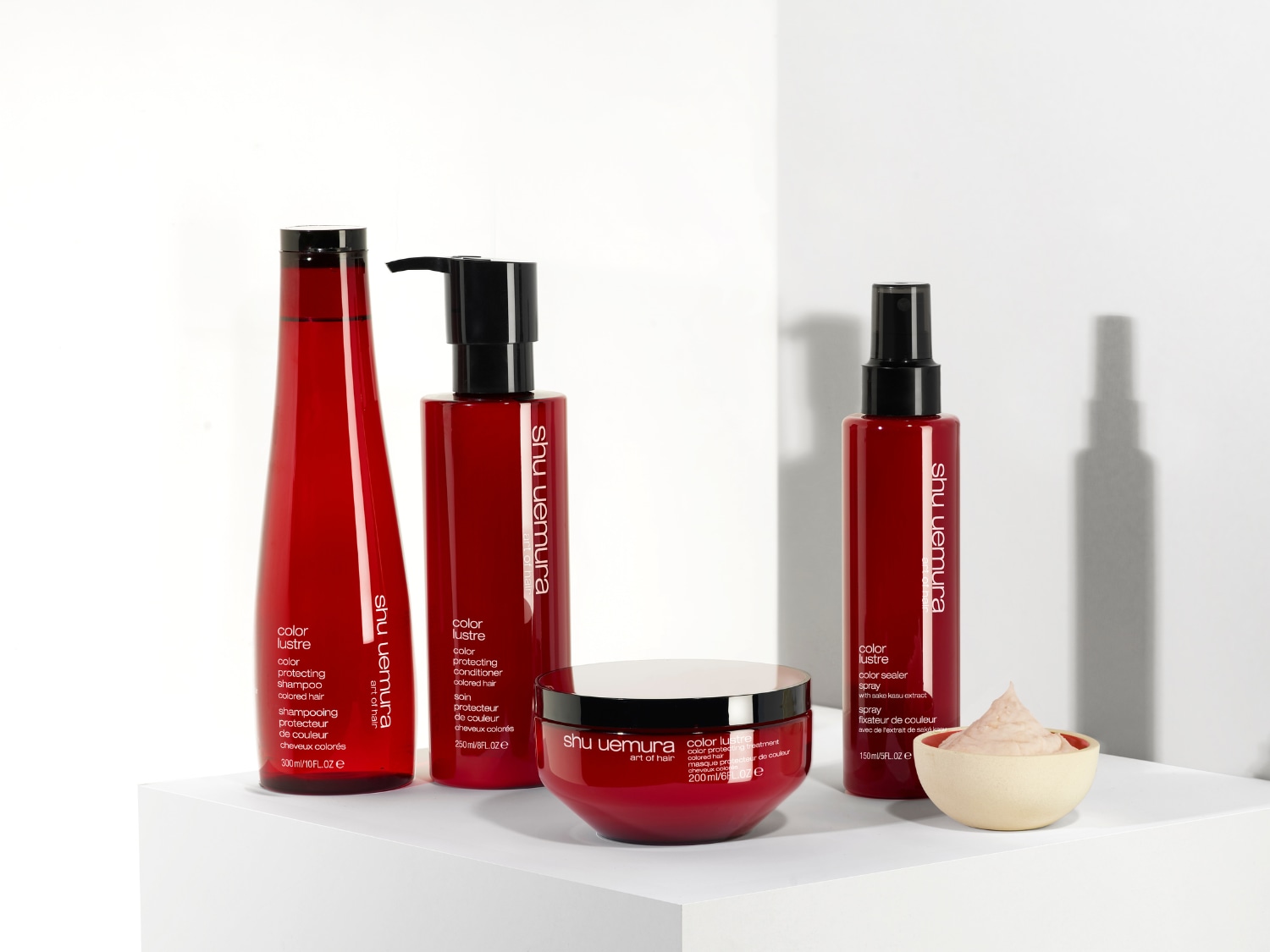 Řada produktů Shu Uemura Color Lustre v červených obalech, včetně šamponu, kondicionéru, masky a spreje pro ochranu barvy vlasů.