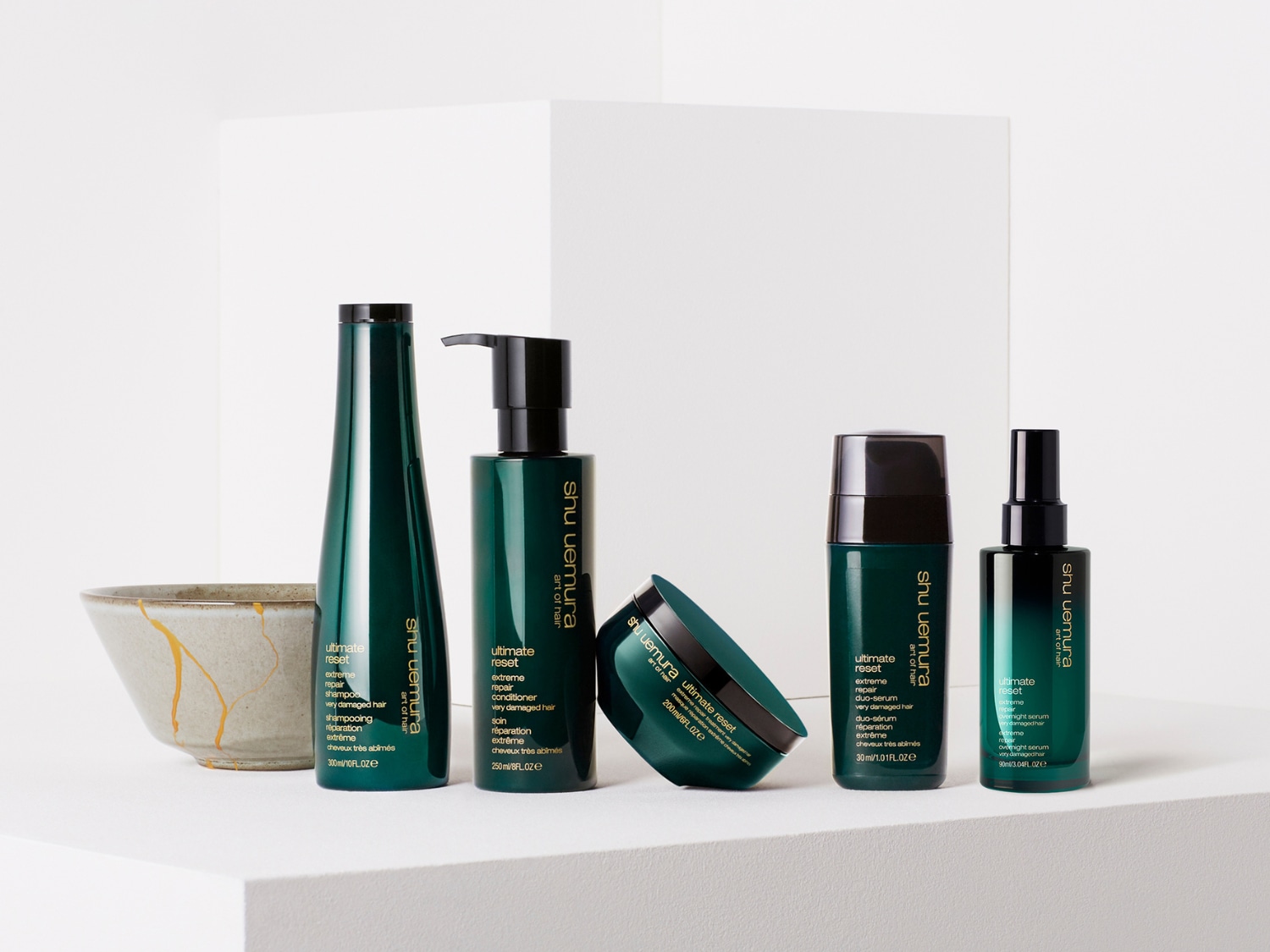 Řada vlasové kosmetiky Shu Uemura Ultimate Reset v tmavě zelených obalech, která zahrnuje šampon, kondicionér, sérum a masku pro velmi poškozené vlasy.