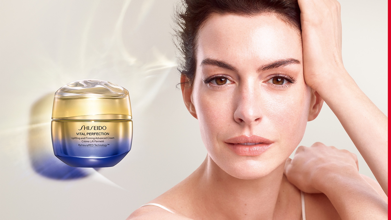 Nahaufnahme einer Frau mit heller Haut neben einem Tiegel Shiseido Vital Perfection Lifting und Firming Advanced Cream mit goldfarbenem Deckel und blauem Unterteil.