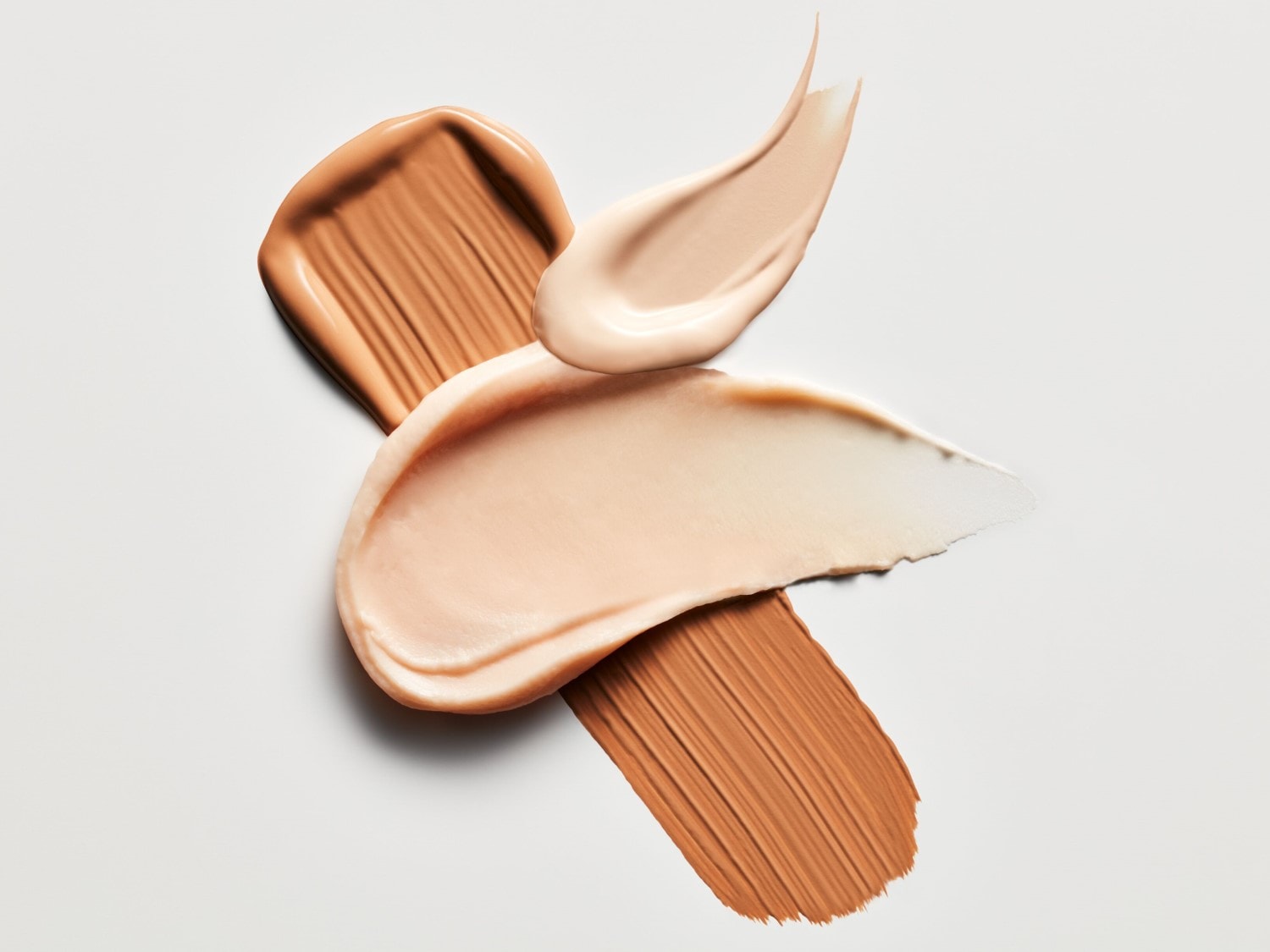 Gros plan sur des échantillons de fond de teint crémeux dans des tons beige et marron, offrant un aperçu des textures et des couleurs disponibles.