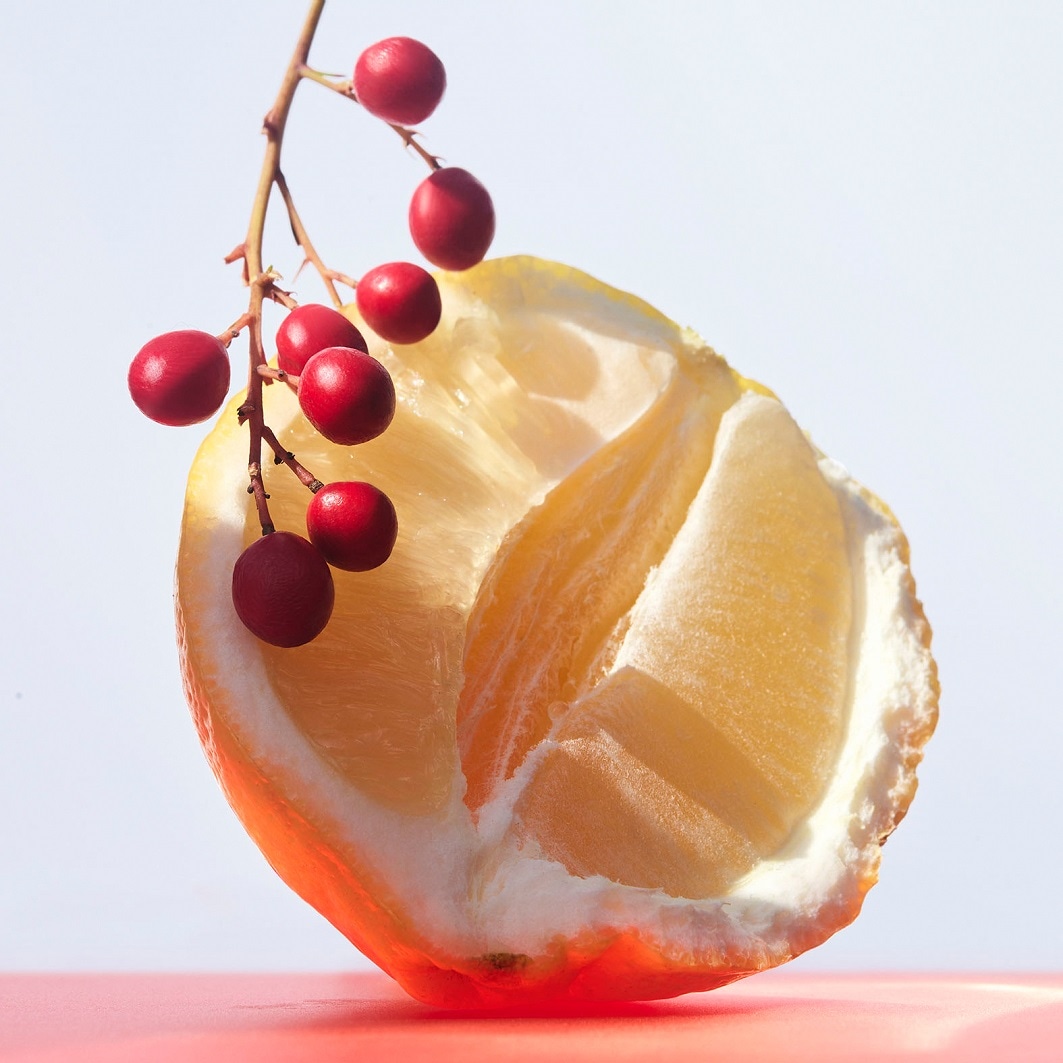 Eine halbe Zitrone mit einem Zweig roter Beeren, die Frische und Natürlichkeit suggerieren.