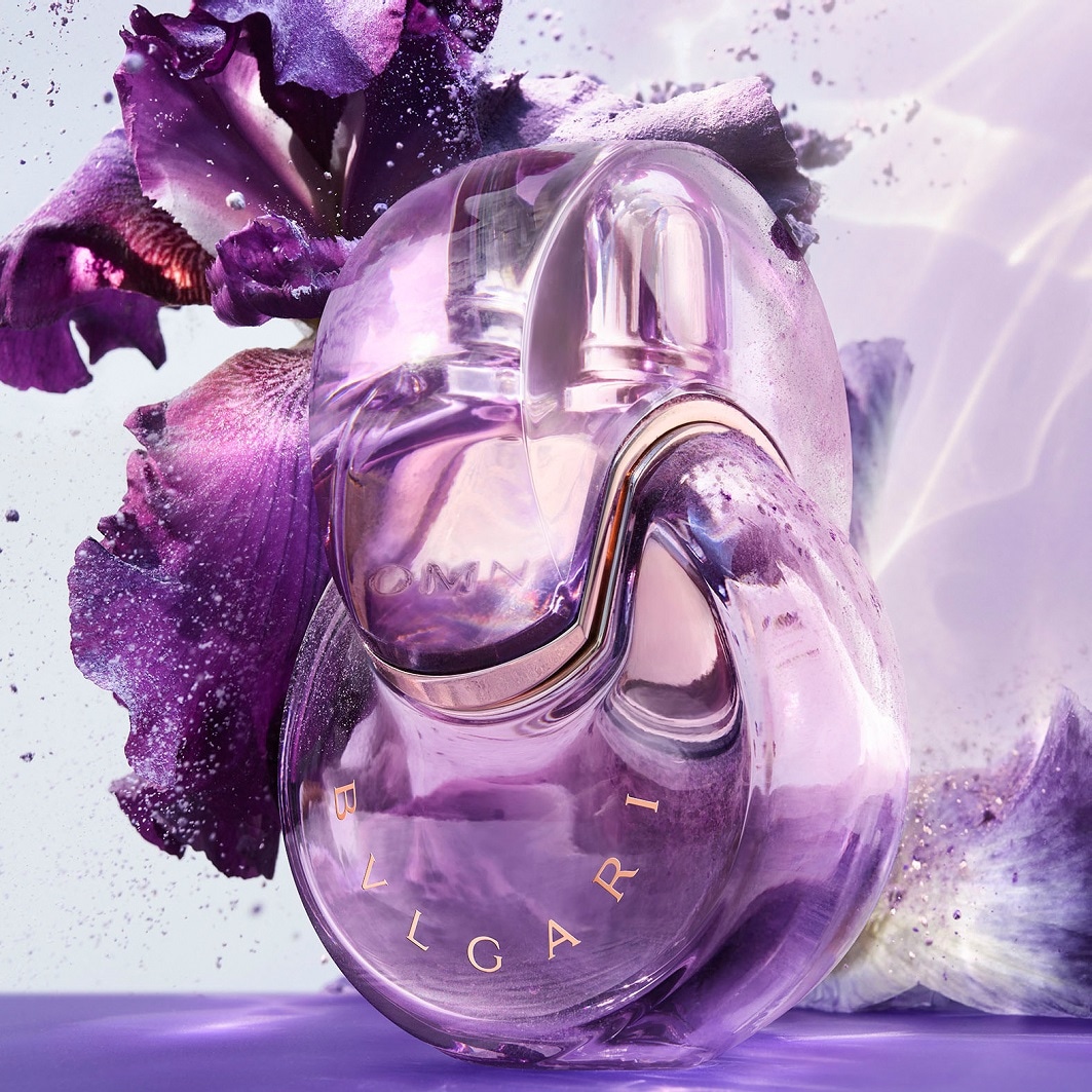 Nahaufnahme des Bvlgari-Parfums Omnia Amethyste, dessen Flakon in zarten Lilatönen gehalten ist und von einer lila Irisblüte umgeben wird.