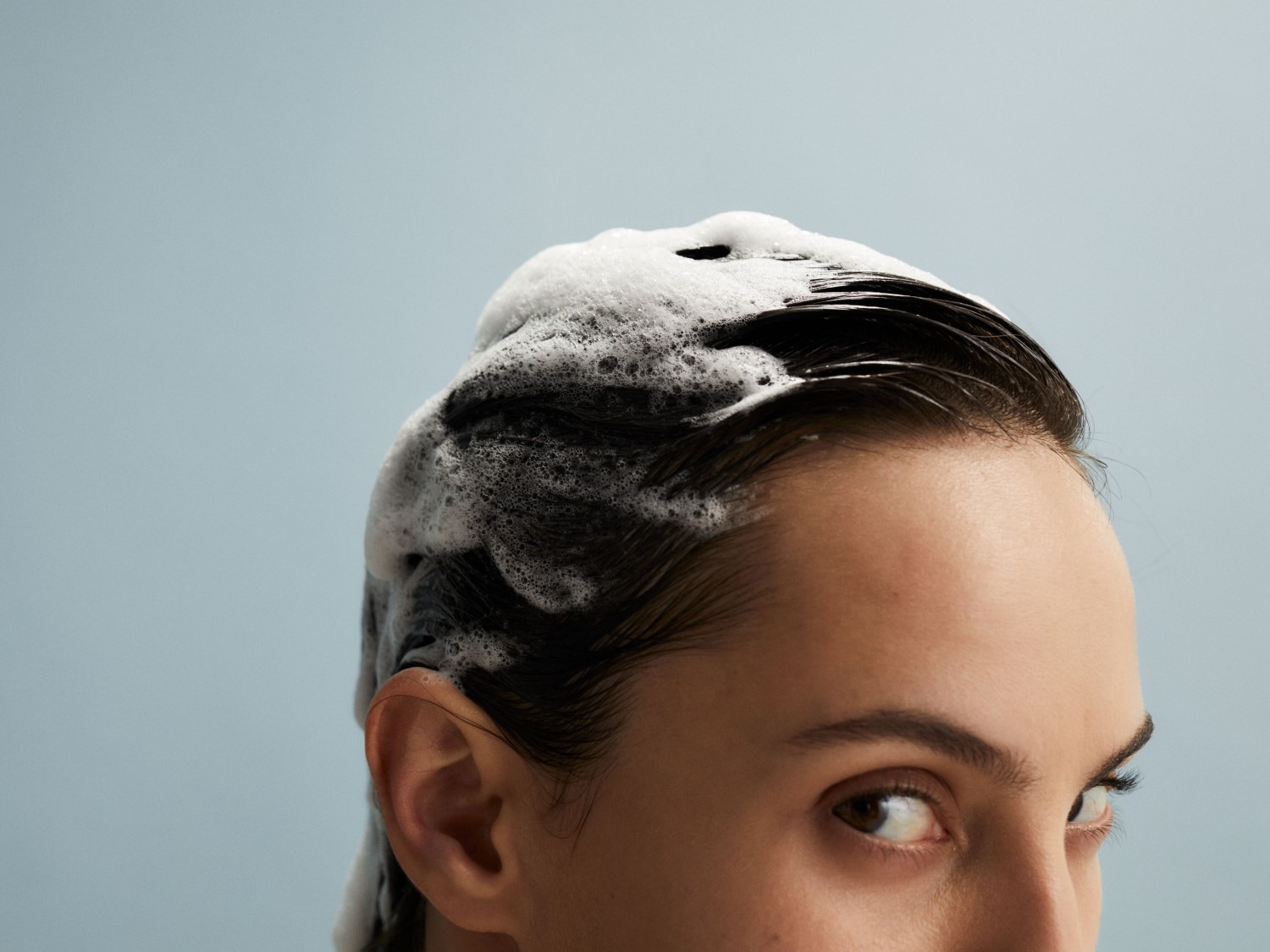 Gros plan sur une femme se lavant les cheveux avec un shampooing moussant, les cheveux mouillés et brillants.