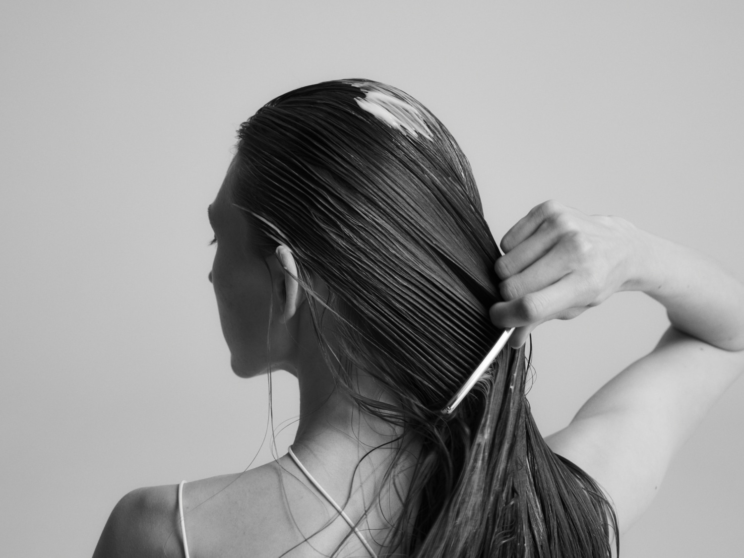 En noir et blanc, une femme démêle ses longs cheveux mouillés avec un peigne, vue de dos.
