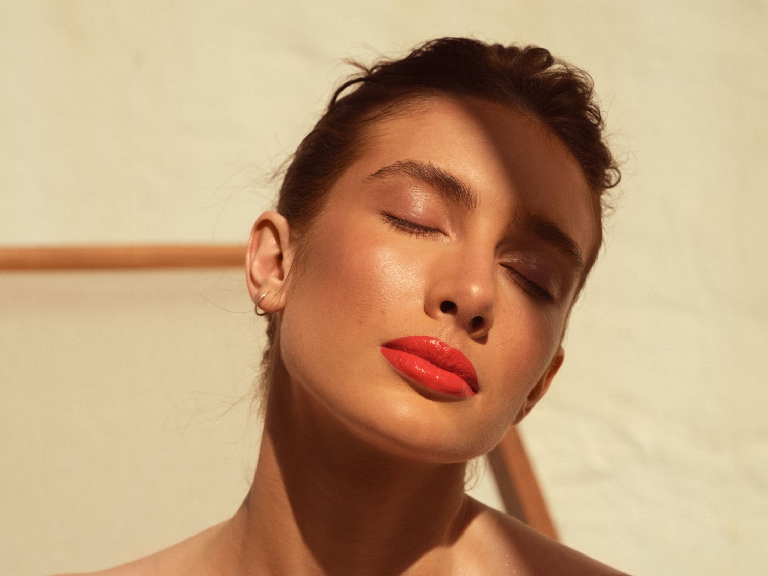 Nahaufnahme einer Frau mit geschlossenen Augen und glänzenden roten Lippen, die im sanften Licht erstrahlen.