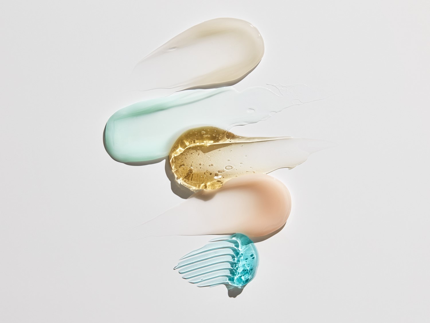 Verschiedene Texturen von Hautpflegeprodukten in Weiß, Türkis, Gold, Pfirsich und Blau sind aufgetragen, um die Vielfalt und Wirksamkeit der Produkte hervorzuheben.