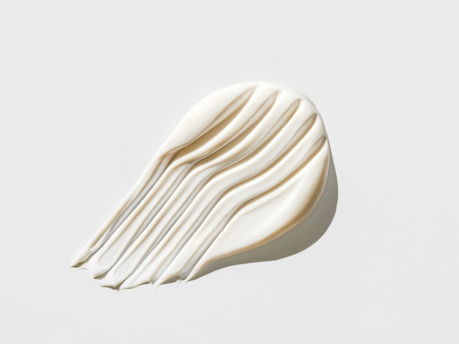 Nahaufnahme eines cremefarbenen Kosmetikprodukts mit glatter, glänzender Textur, das in sanften Wellen aufgetragen wurde.