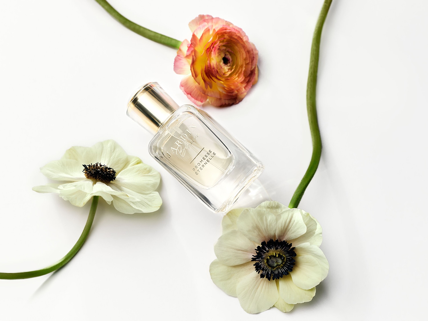 Ein klares Parfümflakon von Jardin Bohème, umgeben von zarten weißen und orangefarbenen Blumen, verspricht einen ewigen Duft.